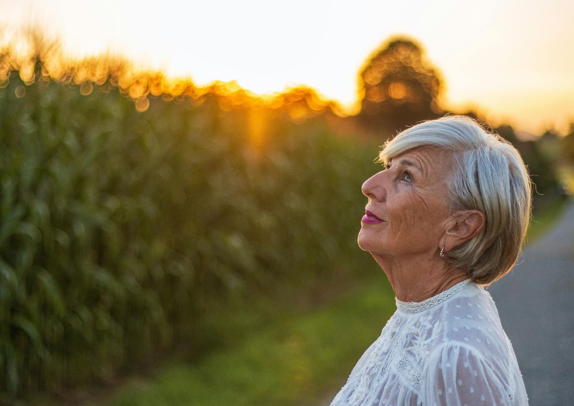 A smiling older woman looking out of a window without glasses, relaxed and content